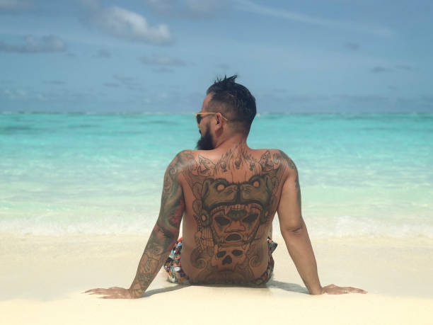 Tattooed Man Sitting By The Sea On The Tropical Beach On Maldives.